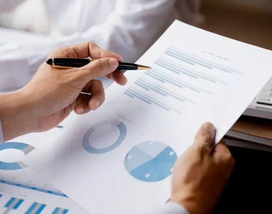 Image showing hands of a man who's holding a pen and looking over reports with charts
