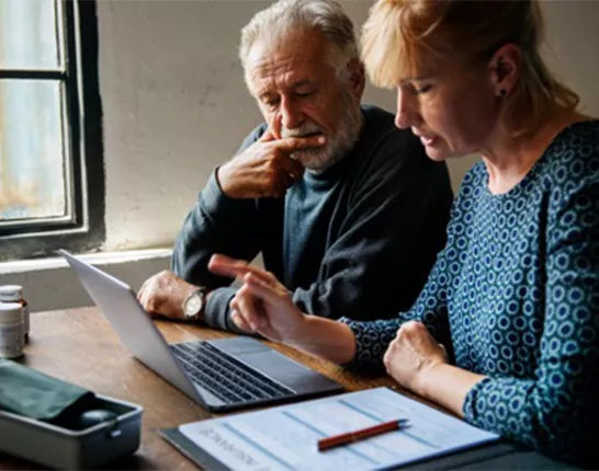 An older man sitting with a middle aged woman looking at a computer