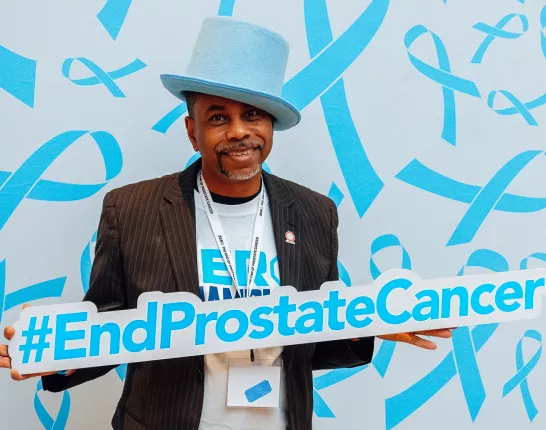 An African American man with a blue tophat holding a sign End Prostate Cancer