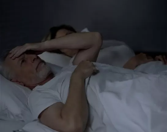 A man laying in bed looking distressed and a woman next to him