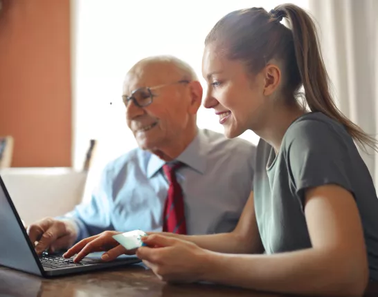 A younger woman helping an elderly man by using a laptop