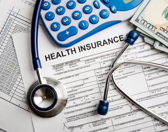 An image of a desk with papers, stethoscope and calculator on it