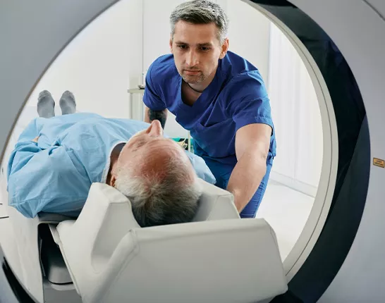Healthcare worker assisting man into an imaging machine