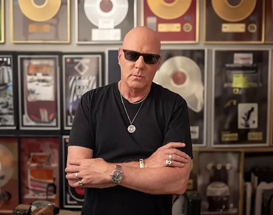 Jay Jay French standing with his arms crossed in front of a wall of records.