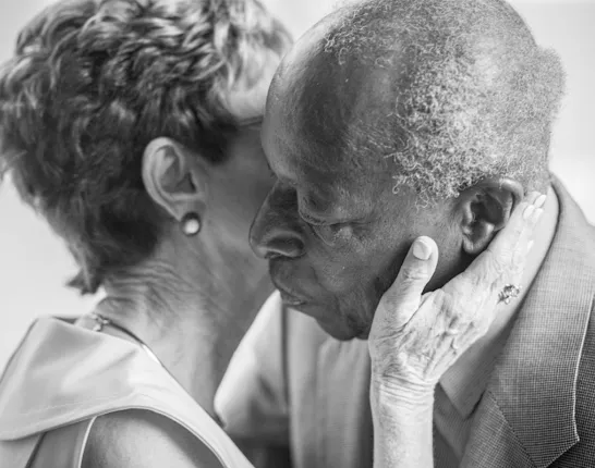 A black and white photo of a senior couple having an intimate moment as she kisses his cheek