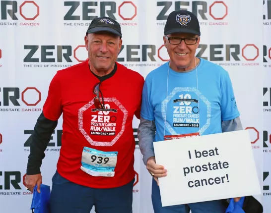 Two men in sports gear holding a "I beat cancer" sign