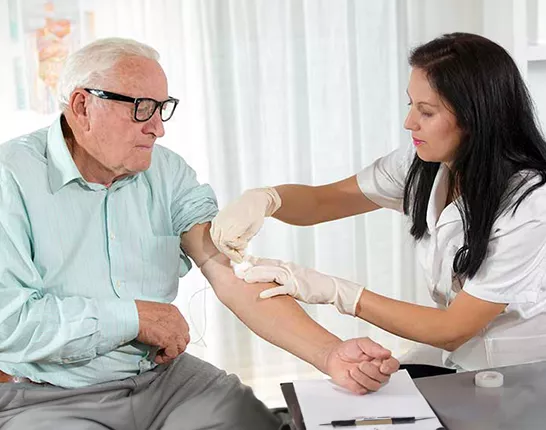 A senior man with his sleeve rolled up while a doctor performs a blood draw