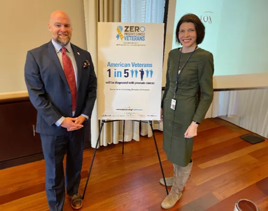 Jamie Bearse and a woman by a sign that says "1 in 5 Veterans will be diagnosed with prostate cancer"