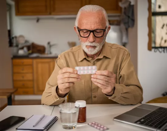 A man sitting at a kitchen table looking at pills