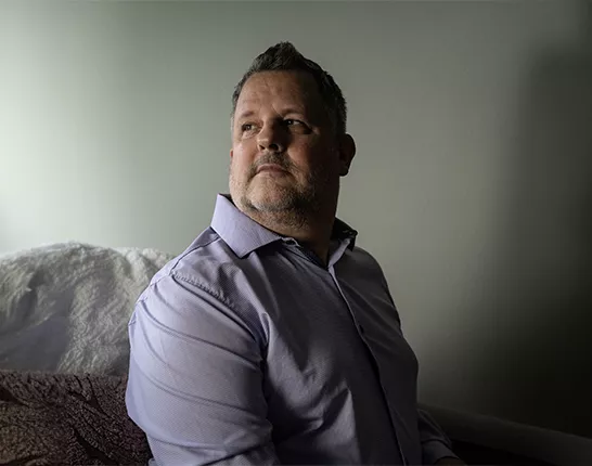 David Weigand, a Prostate Cancer Patient, sitting on a bed and looking over his right shoulder