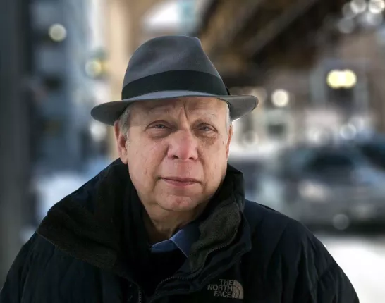 A middle-aged man with a hat and a dark coat