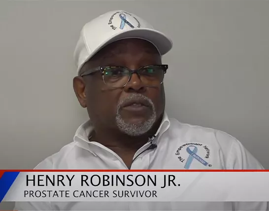 A black man wearing a white polo shirt and white hat, both have a blue ribbon with that says "I Survived". The ribbon is surrounded by text that says "The Empowerment Network". There is also a banner across the bottom that says "Henry Robinson Jr. Prostate Cancer Survivor".