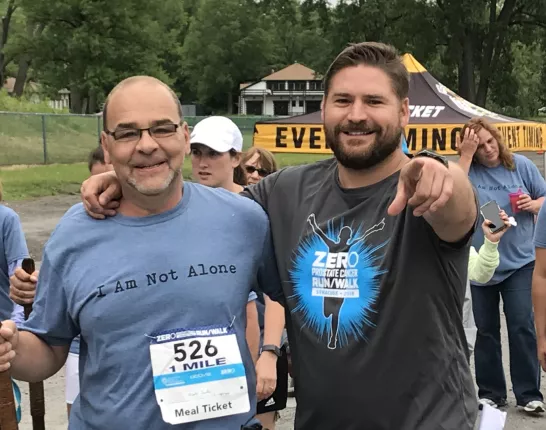 Two men at a run walk event one wearing "I Am Not Alone shirt" and the other pointing at the camera