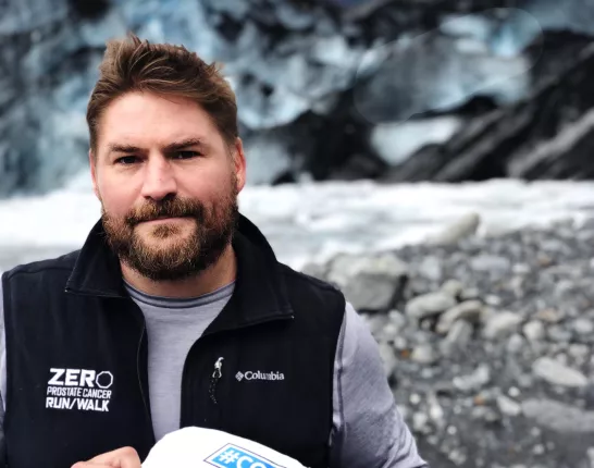 Man looking at the camera in an artic tundra holding up a reasons I fight sign