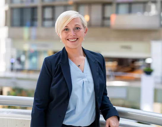 Blonde woman with very short hair wearing a light blue shirt and dark blue blazer