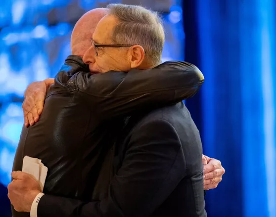 Two men hugging at Bold for Blue Awards wearing black with a blue background