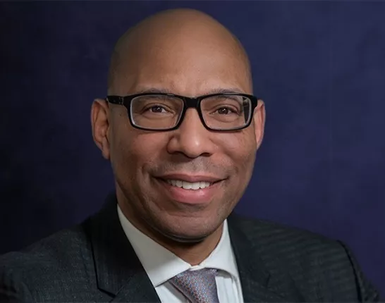 Black man wearing glasses and a black suit posing for headshot