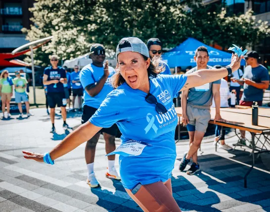 A woman with a backwards hat wearing a Run/Walk shirt standing with her arms out in a silly position