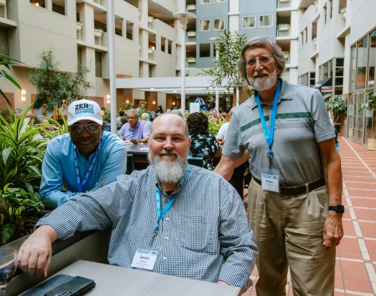 Three men sit together in a courtyard and smile at the camera.