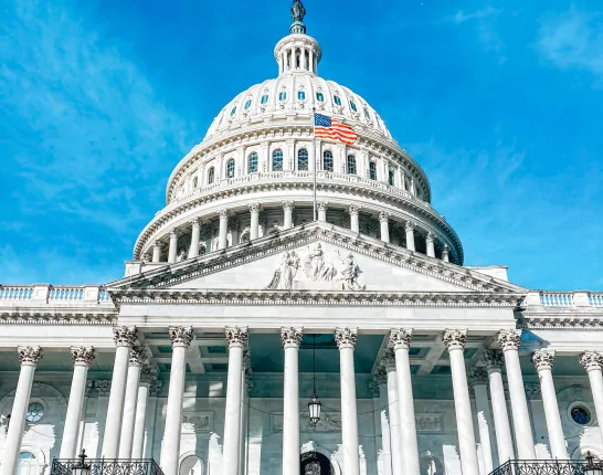 The U.S. Capitol building under a clear blue sky, featuring its iconic dome and American flag.