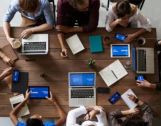 Group of people at wood desk with computers and coffee