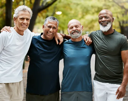 Four men standing with arms around each other shoulder to shoulder smiling
