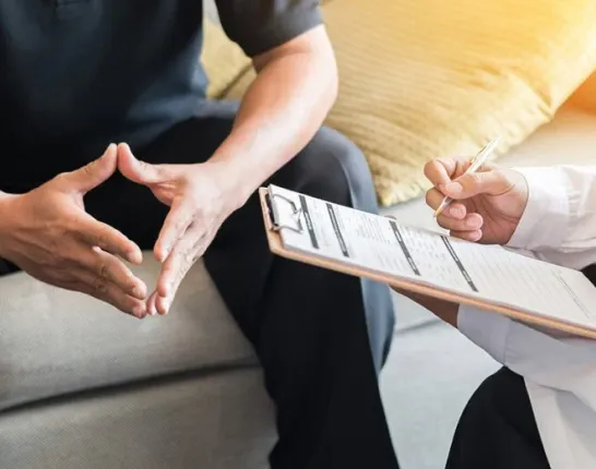 Image of hands of a patient and doctor. The doctor is holding a clipboard and appears to be consulting with the patient.
