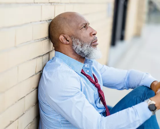 Black man sitting on the ground against a brick wall looking distressed