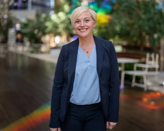 ZERO President & CEO, Courtney Bugler, standing in a room with wood floors, trees in the back, and a lighting casting a rainbow on the ground behind her