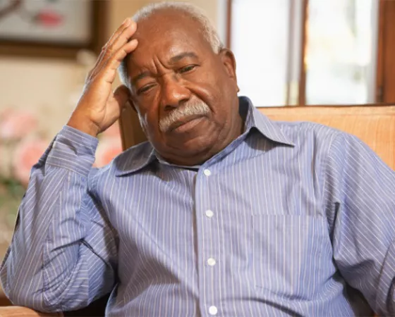 An older black man with his head on his hand as he slumps in a chair