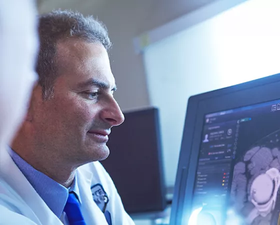 A man in a doctor's coat looking and radiographic imaging of a prostate on a computer