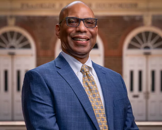 Brian Bragg, Chief Mission Officer, a Black man in a blue suit and yellow checkered tie standing in front of a brick building