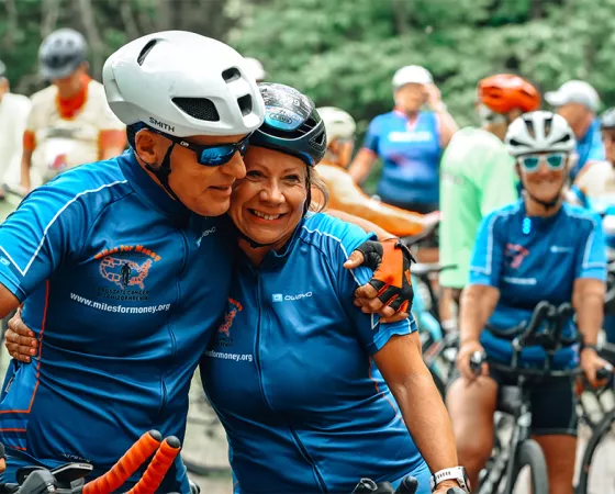An older couple in cycling jerseys and helmets embracing while surround by many onlooking cyclists
