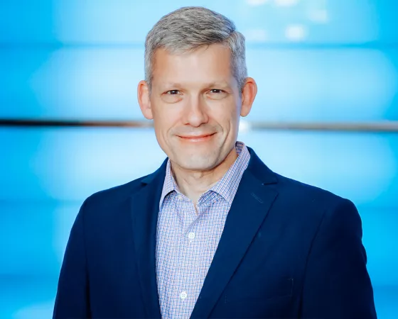 A white man with gray hair wearing a blue suit against a blue background