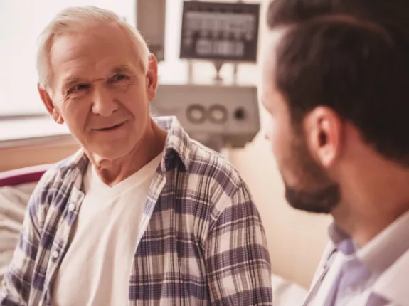 A male patient sitting on a hospital bed speaking with his doctor