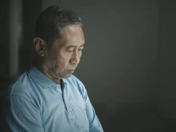 An asian man in a dark room looking down at the ground