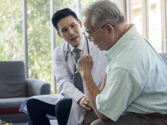 A young asian doctor speaking with an older male on a couch