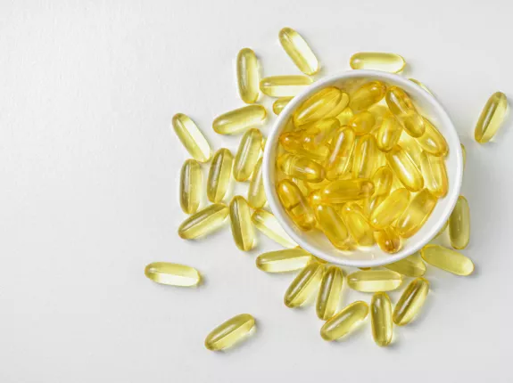 white bowl of yellow pill capsules overfilled onto white background