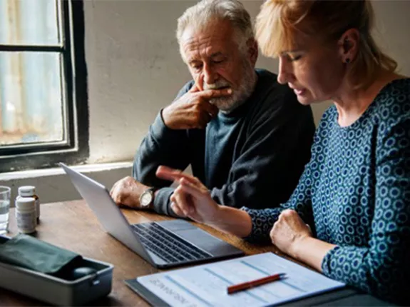 An older man sitting with a middle aged woman looking at a computer