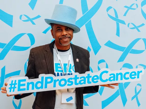 An African American man with a blue tophat holding a sign End Prostate Cancer