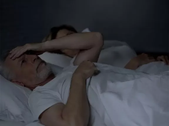 A man laying in bed looking distressed and a woman next to him