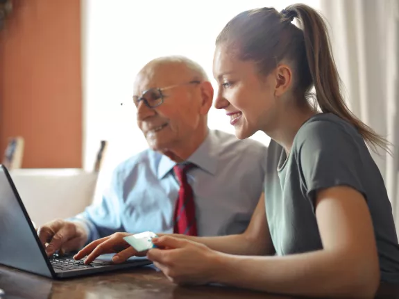 A younger woman helping an elderly man by using a laptop