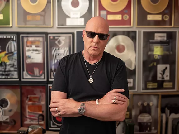 Jay Jay French standing with his arms crossed in front of a wall of records.