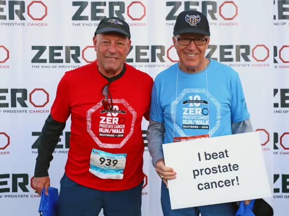 Two men in sports gear holding a "I beat cancer" sign