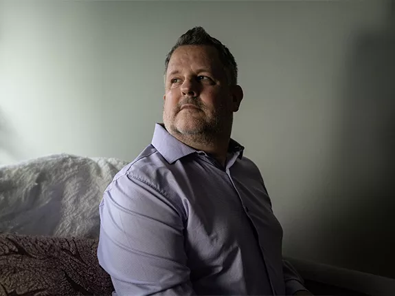 David Weigand, a Prostate Cancer Patient, sitting on a bed and looking over his right shoulder