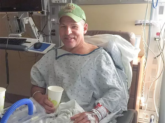 Cancer patient, Scott Freitag, sitting in a hospital bed hooked up to machines but smiling
