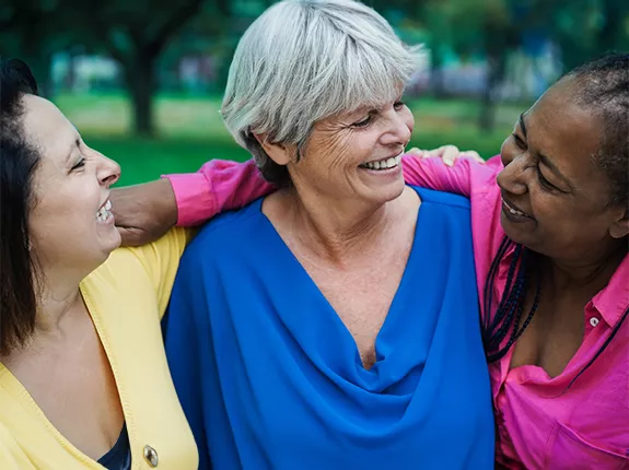 A Latino, white, and Black woman standing with their arms around each other