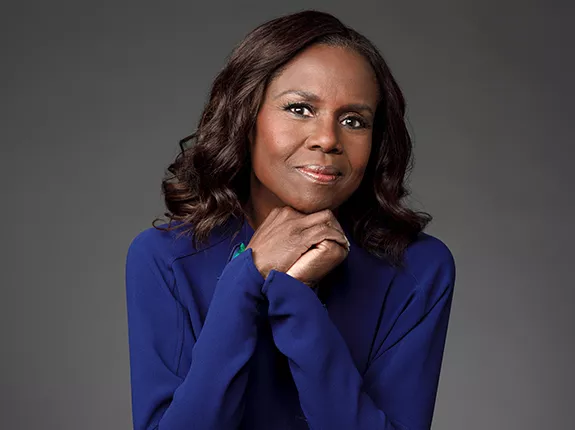 A black woman wearing a blue shirt holding her hands under her chin