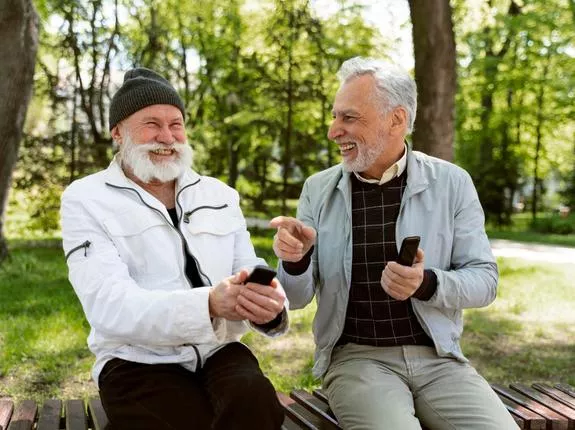 Two men laughing in park sitting on bench