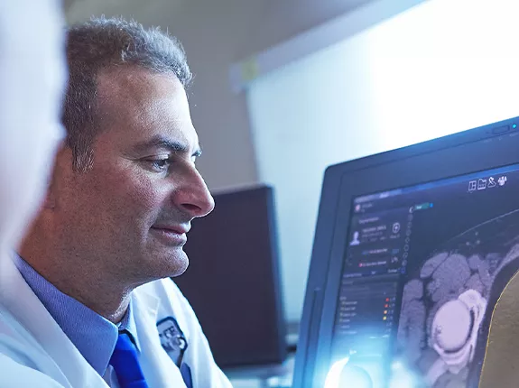 A man in a doctor's coat looking and radiographic imaging of a prostate on a computer